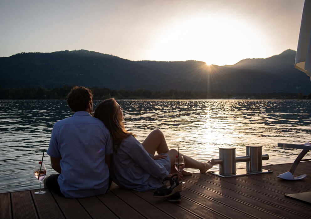 Verliebtes Pärchen genießt ihr Romantik Urlaub auf einem Steg am Wolfgangsee und beobachtet den Sonnenuntergang