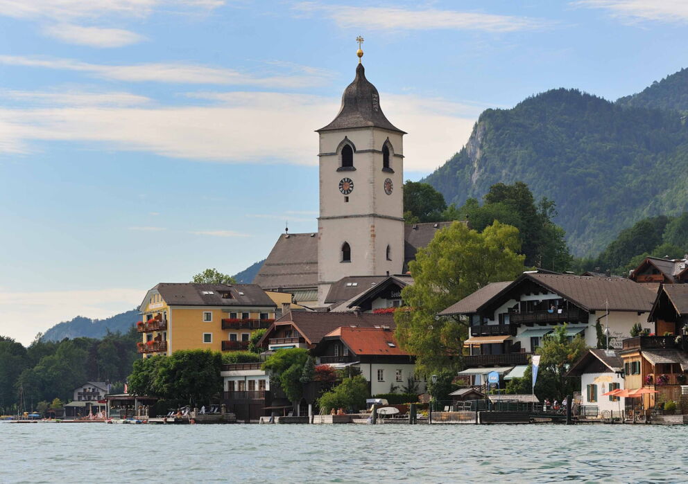 Kirchturm und Dorf von Sankt Wolfgang mit dem Wolfgangsee und dem Gebirge im Hintergrund