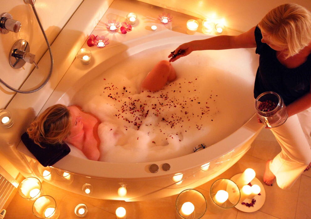 Frau in einer befüllten Badewanne mit Kerzen und roten Blüten