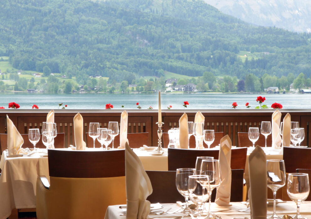 Gedeckte Tische auf einer freien Terrasse eines Restaurants im Weissen Rössl mit Blick auf den Wolfgangsee