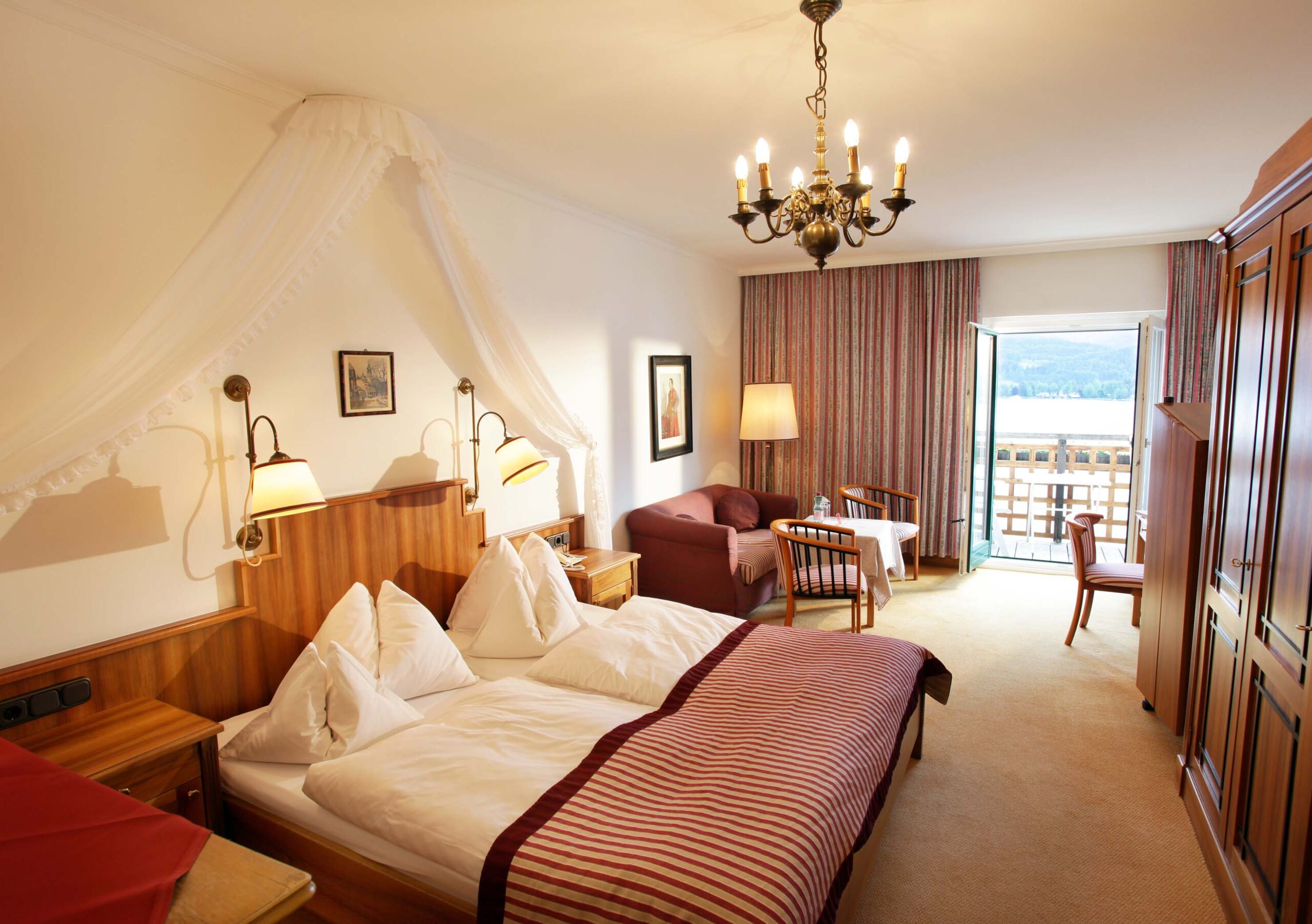 Zimmer im Weissen Rössl im Stil der 50er Jahre mit Balkonsicht uriger Nachttischbeleuchtung auf den Wolfgangsee, schönem Deckenkronleuchter und gemütlichem Bett