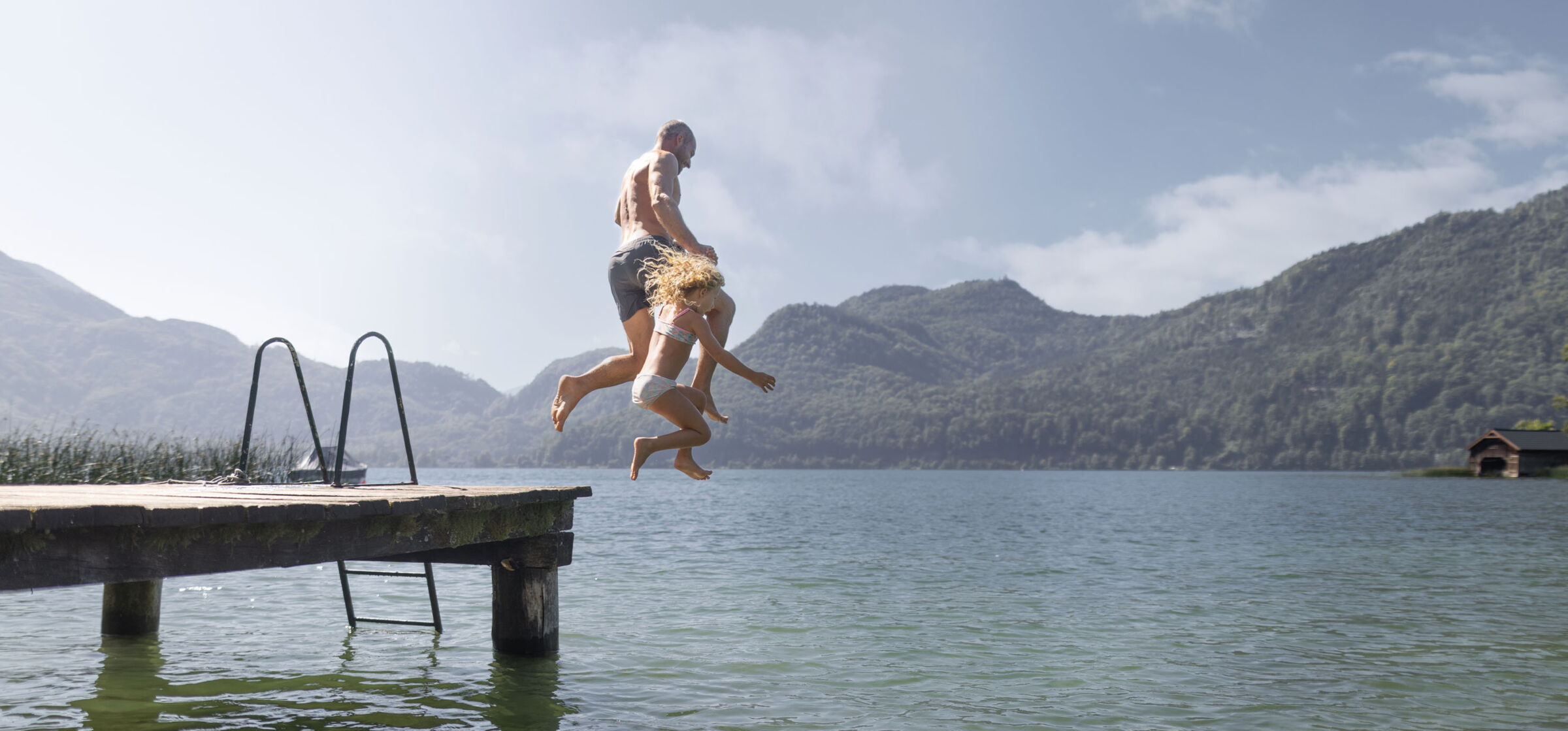 Vater und Tochter springend von einem Steg in den Wolfgangsee