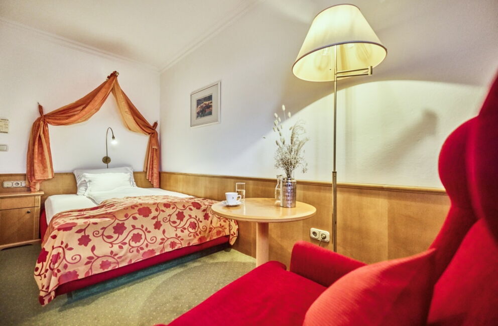 Einzelzimmer im Romantik Hotel Im Weissen Rössl am Wolfgangsee mit Bett, rotem Sessel, Stehlampe und kleinem Tisch.