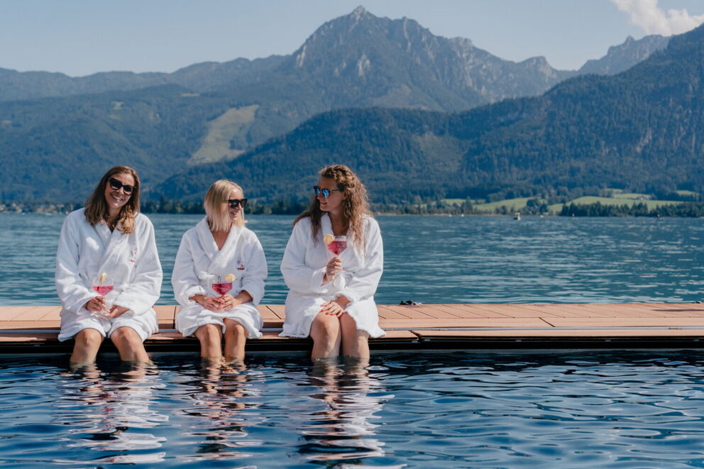 Drei Freundinnen sitzen mit einem  Getränk in der Hand am Seebad und unterhalten sich beim Wellness am Wolfgangsee.