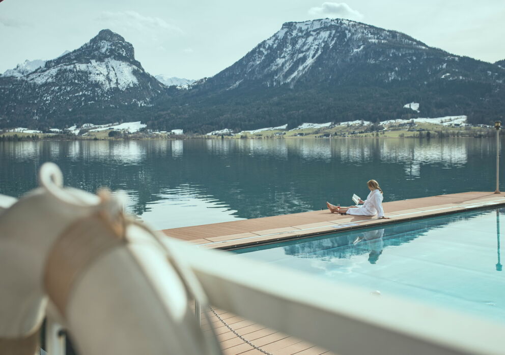 Lesende Frau am beheizten Seebad mit umliegender angezuckerter Berglandschaft