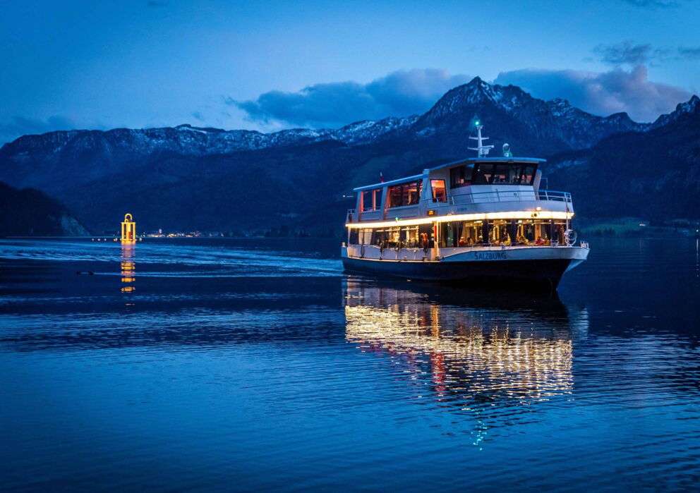 Schifffahrt im Winter am Wolfgangsee mit Sicht auf die angezuckerten Berge und einer großen Adventskerze mitten am See