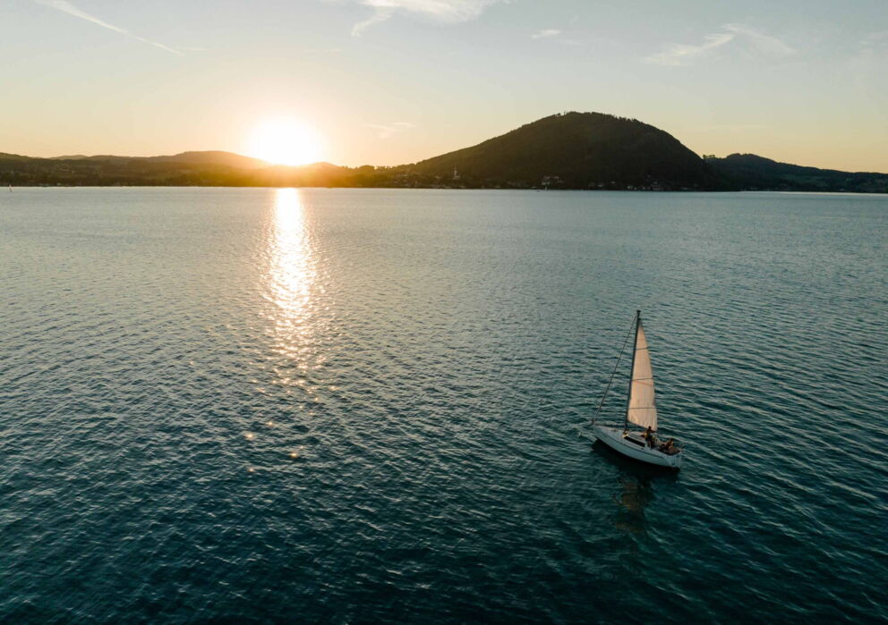 Ein Segelboot mitten in dem großen schimmernden Wolfgangsee während des Sonnenuntergangs