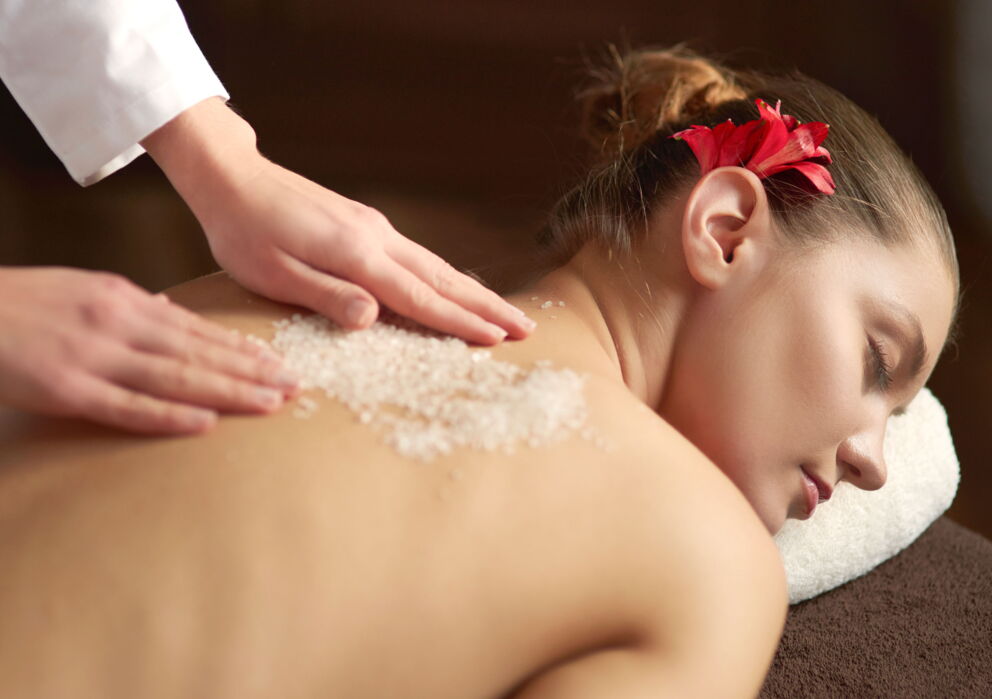 Frau bei einer Massage mit Salz am Rücken und einer Blume im Haar