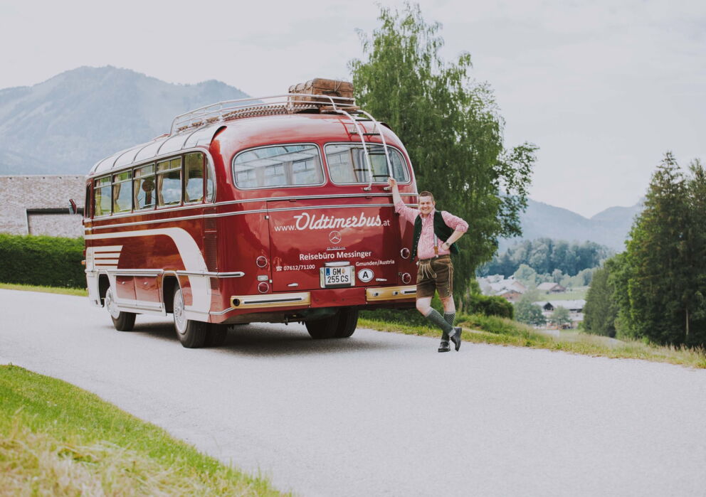 Traditionally Austrian dressed man in front of a red vintage bus