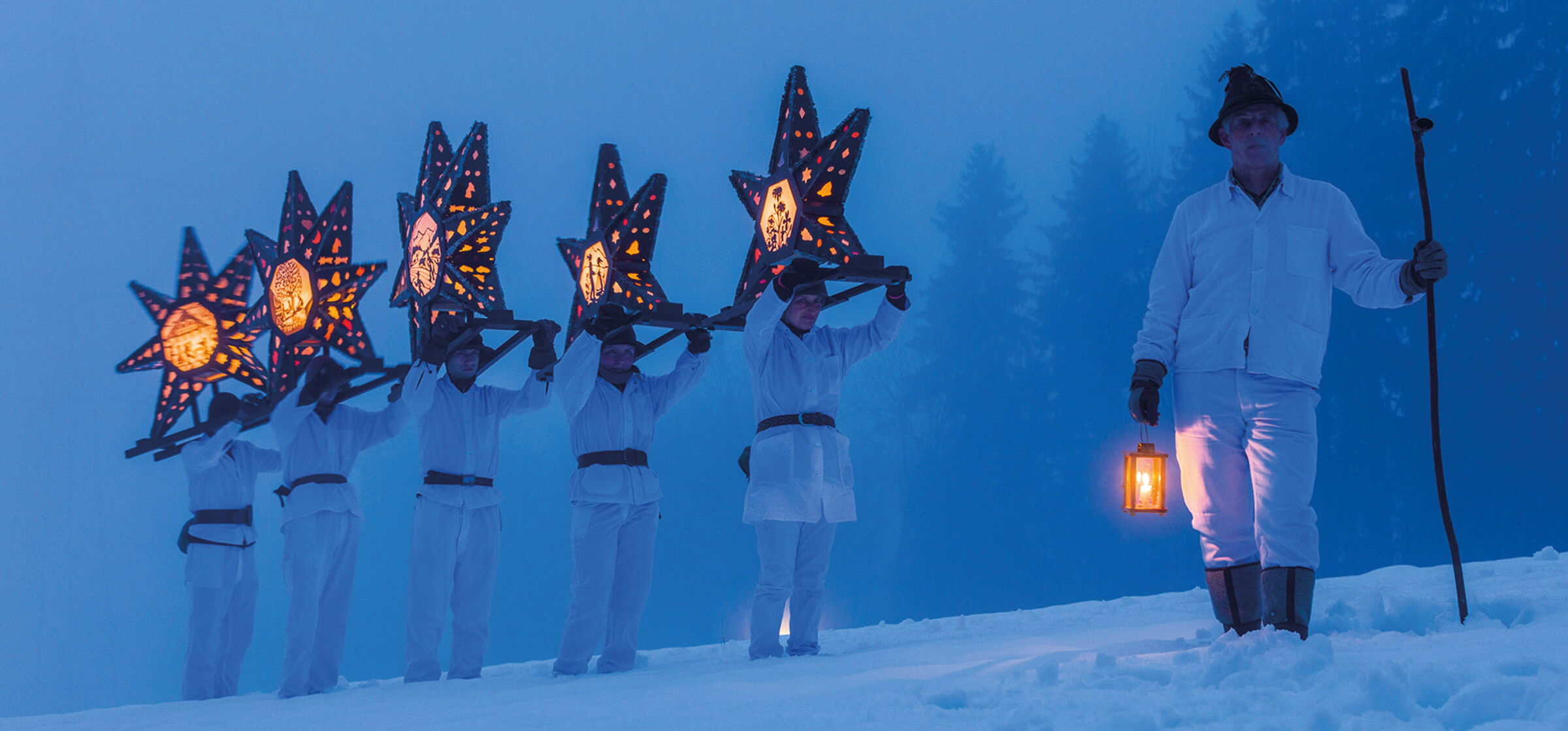 Mehrere Menschen stehen im Schnee und tragen Laternen