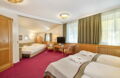 Familienzimmer im Romantik Hotel Im Weissen Rössl am Wolfgangsee mit Doppelbett, separatem Schlafbereich, Fernseher, Schreibtisch, Kleiderschrank, Sitzgelegenheit und klassischer Holzausstattung.