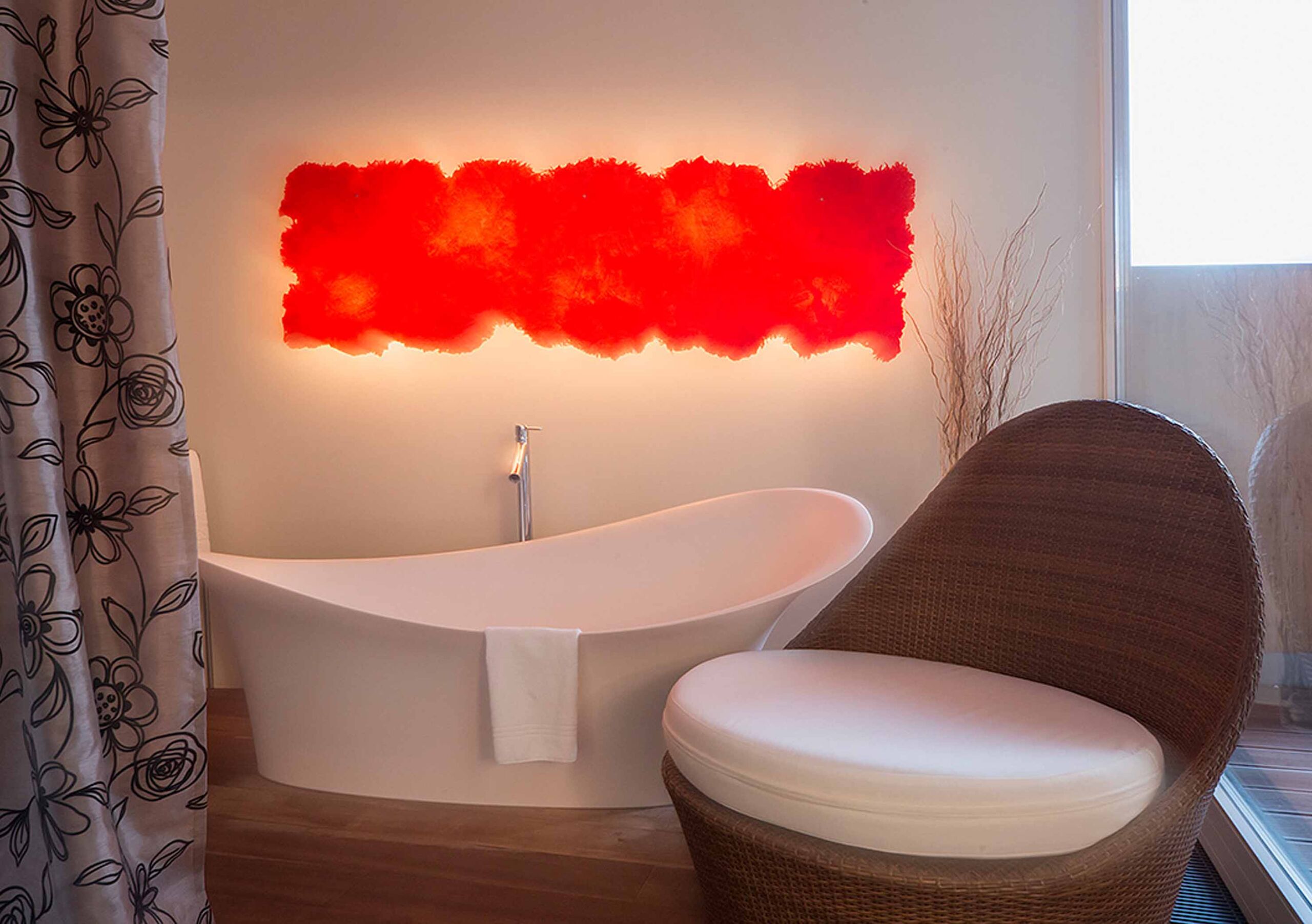 Frei stehende offene Designbadewanne mit schöner roten Wandleuchte und gemütlichen Wellness Sessel