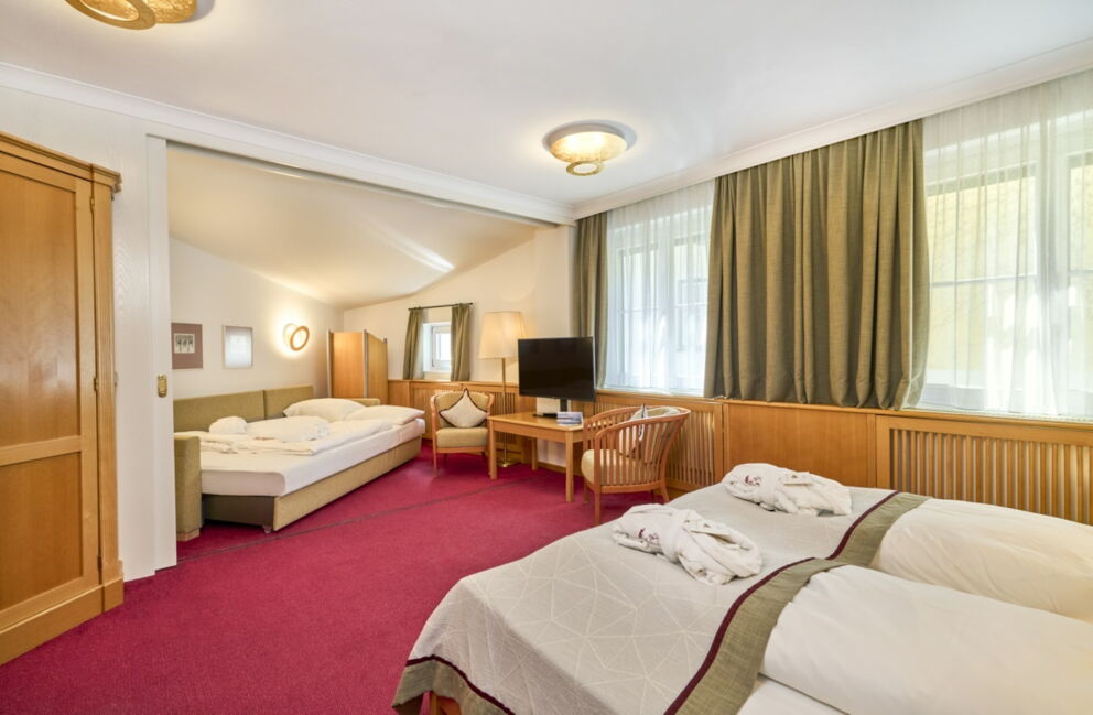 Familienzimmer im Romantik Hotel Im Weissen Rössl am Wolfgangsee mit Doppelbett, separatem Schlafbereich, Fernseher, Schreibtisch, Kleiderschrank, Sitzgelegenheit und klassischer Holzausstattung.