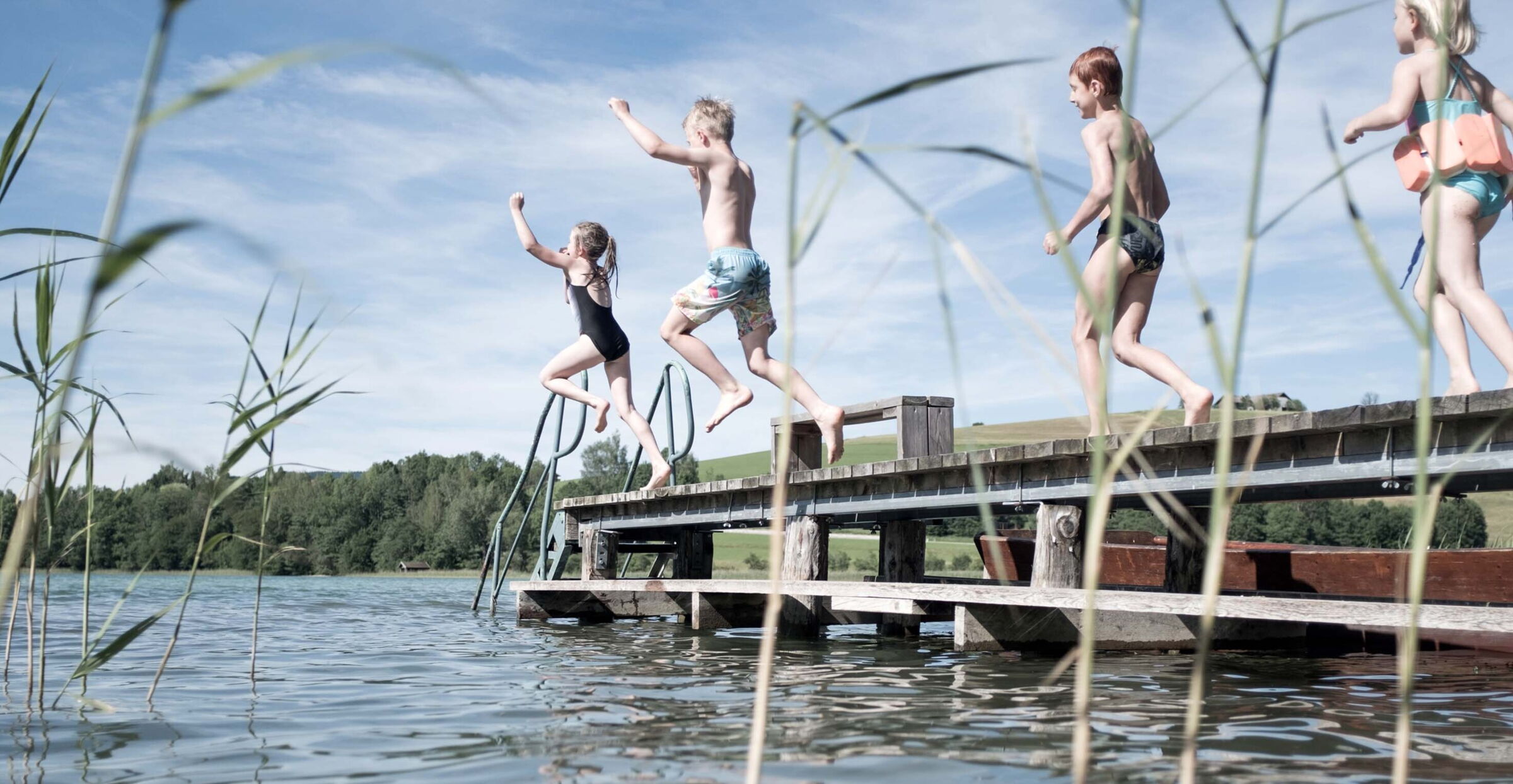 Mehrere Kinder springen von einem Holz Steg ins Wasser