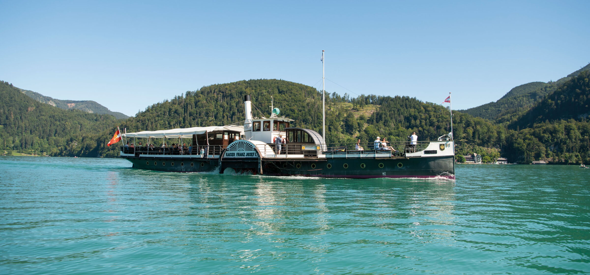 Fahrendes Schiff auf dem türkis glänzendem Wasser des Wolfgangsees