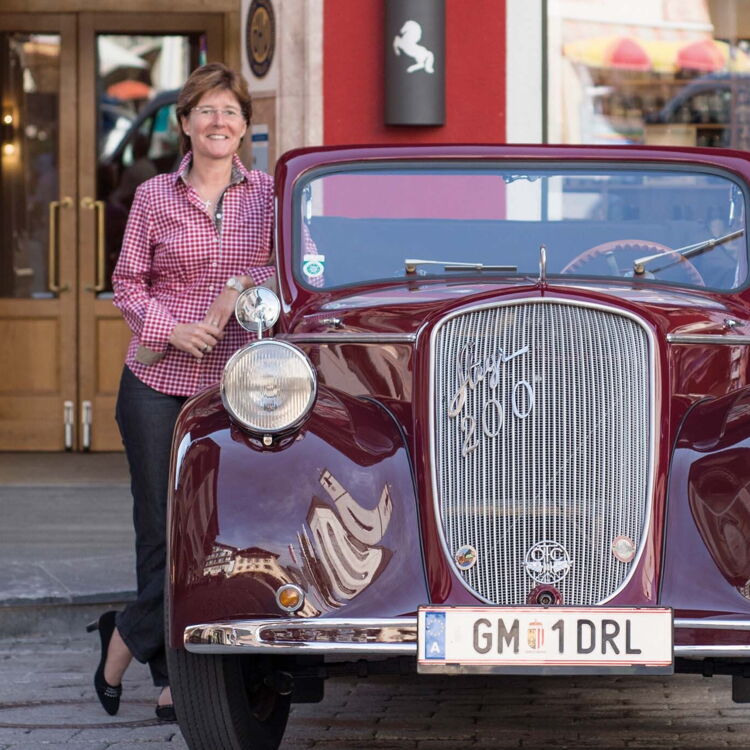 Ein Mann und eine Frau mit einem roten Oldtimer vor dem Eingang des Hotels im Weissen Rössl