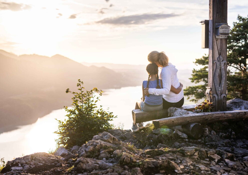 Mutter und Tochter sitzend auf einem Berggipfel mit Aussicht auf den Wolfgangsee