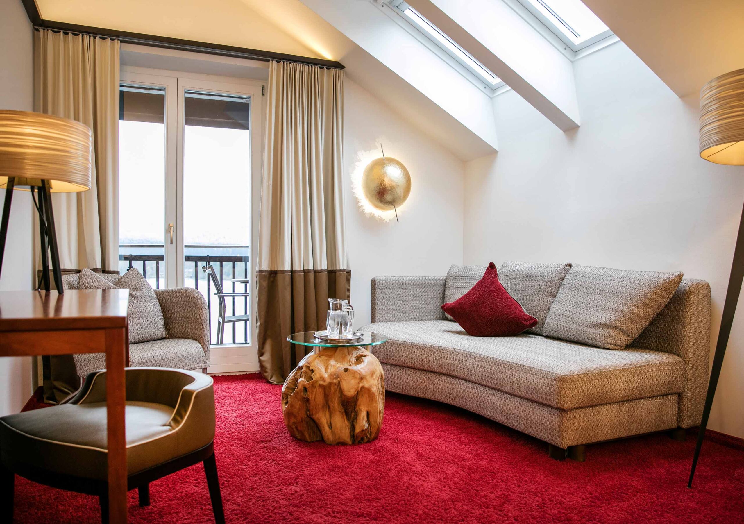 Helles Zimmer mit rotem Teppichboden und moderner Einrichtung verfügt über einen Balkon mit atemberaubendem Blick auf den Wolfgangsee sowie einem gemütlichen Sofa und einem Couchsessel
