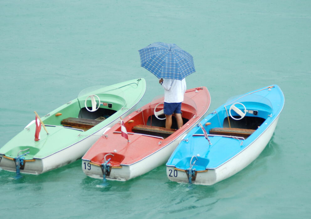 Mann mit einem Regenschirm in einem von drei farbigen Booten am Wolfgangsee