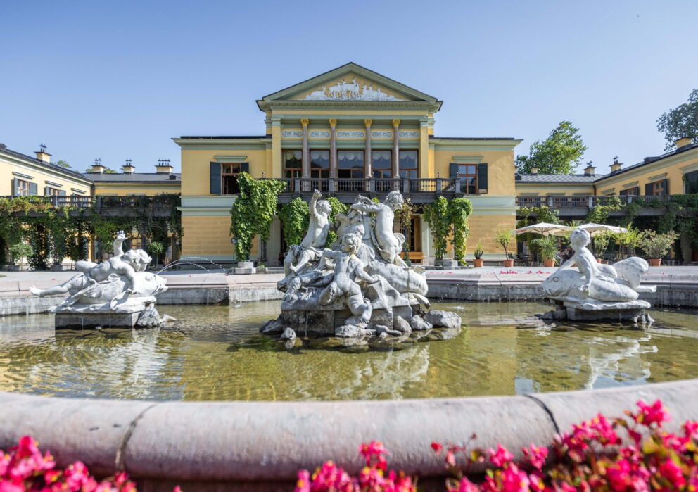 Frontansicht der Kaiservilla in Bad Ischl mit Sicht auf den Brunnen und wunderschönen rosa Blumen