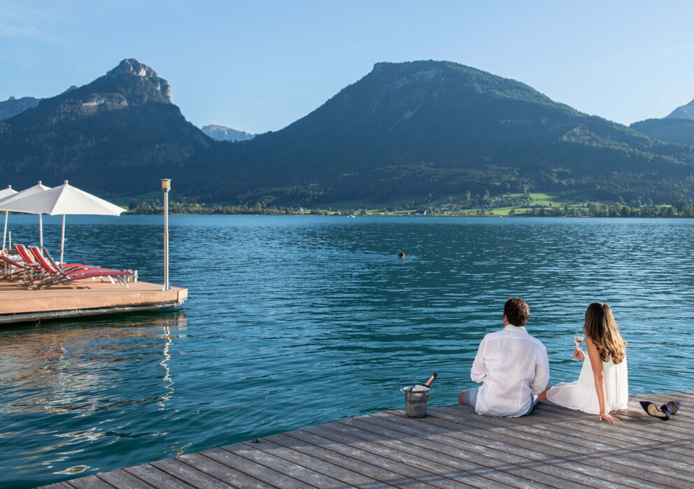 Romantik Urlaub im Weissen Rössl: Verliebtes Pärchen mit einer Flasche Sekt an einem Steg am Wolfgangsee