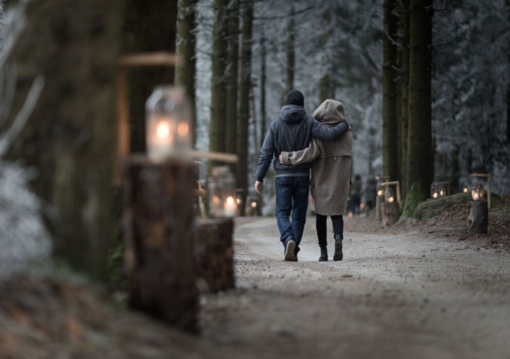 Ein Paar spaziert arm in arm durch einen Wald der mit Laternen erleuchtet wird