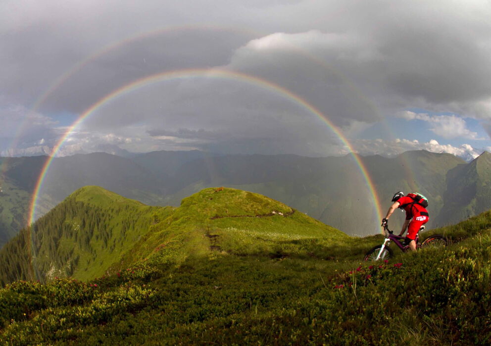 Mann auf dem Fahrrad am Mountainbiken mit Blick auf einen doppelten Regenbogen in den Bergen