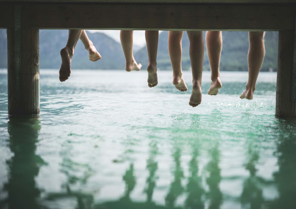 Eine Familie die beim Familienurlaub am See die Beine über den Wasser schwingt am Wolfgangsee.