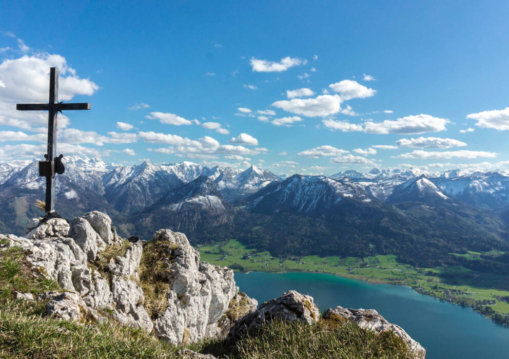 Sicht von einem Gipfel mit Gipfelkreuz auf den Wolfgangsee und der tiefen, teils verschneiten Berglandschaft des Salzkammerguts