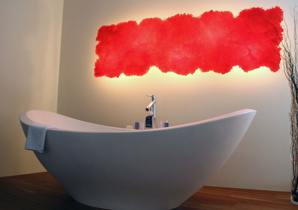 Offen stehende Design Badewanne mit einer kunstvollen roten Wandleuchte im Hintergrund.