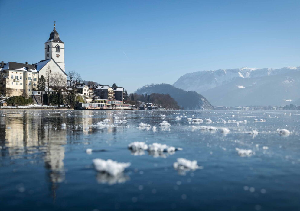 Winterblick auf das Weisse Rössl und den zugefrorenen Wolfgangsee sowie der verschneiten Berglandschaft