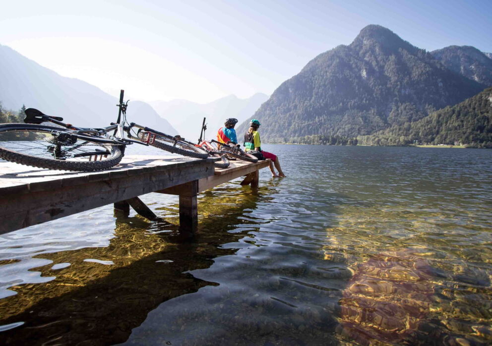 Radfahrer sitzend auf einem Steg am Wolfgangsee mit Blick auf die Berglandschaft des Salzkammerguts