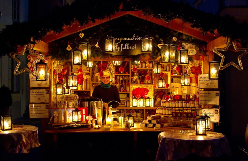 Ein Stand am Adventmarkt im Salzkammergut, beleuchtet mit vielen Laternen. Im Adventmarktstand wird Apfelbrot und weitere regionale Spezialitäten angeboten.