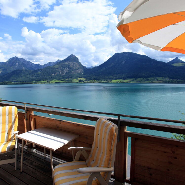Balkon mit Sonnenliegen und einem Sonnenschirm mit Sicht auf den Wolfgangsee