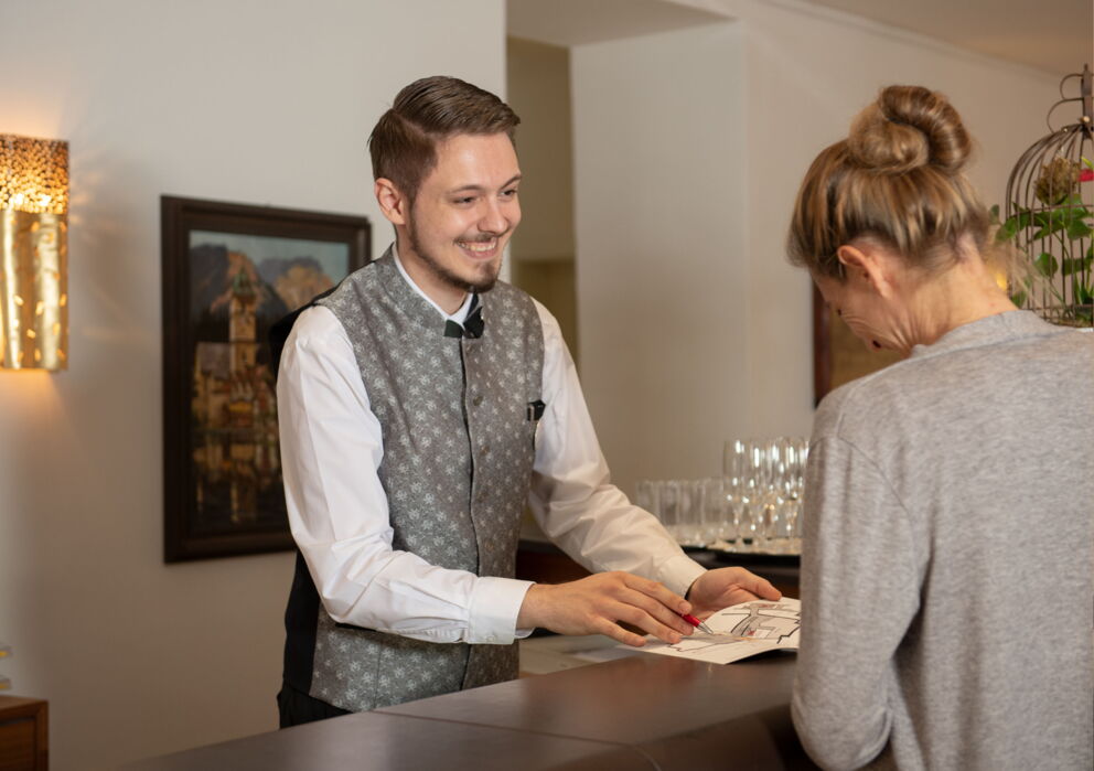 Der Rezeptionist zeigt einem Gast den Hotelplan des Weissen Rössl am Wolfgangsee