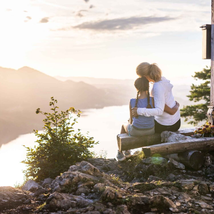 Mutter und Tochter sitzend auf einem Berggipfel mit Aussicht auf den Wolfgangsee