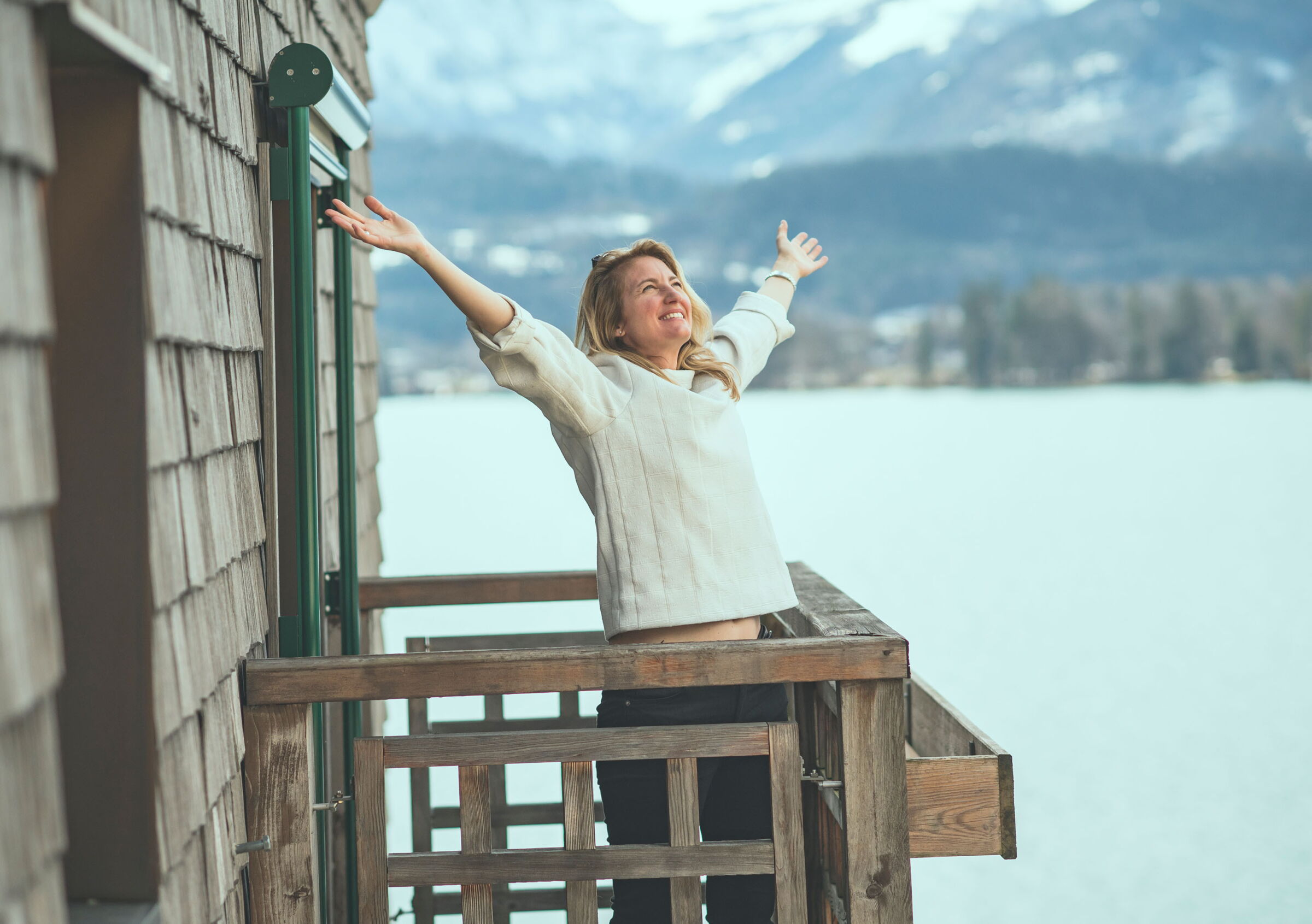 Happy woman with outstretched hands on a balcony with a view of Lake Wolfgang