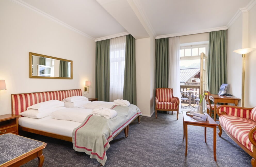 Doppelzimmer im Romantik Hotel Im Weissen Rössl am Wolfgangsee mit Doppelbett, Sofa, Sessel, Schreibtisch, Fernseher, klassischer Einrichtung und Zugang zum Balkon.
