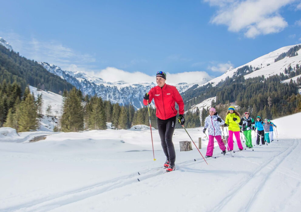 Ein Mann mit Gruppe von Kindern am Langlaufen in der schneebedeckten Berglandschaft