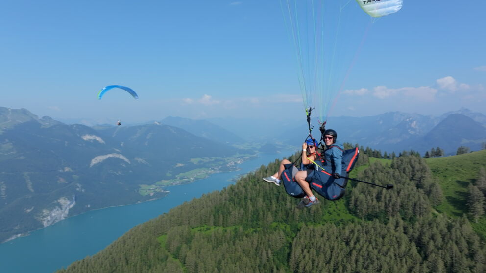 Ein Duo in einem Paragleitschirm fliegt über den Wolfgangsee. ©Flugschule Salzkammergut