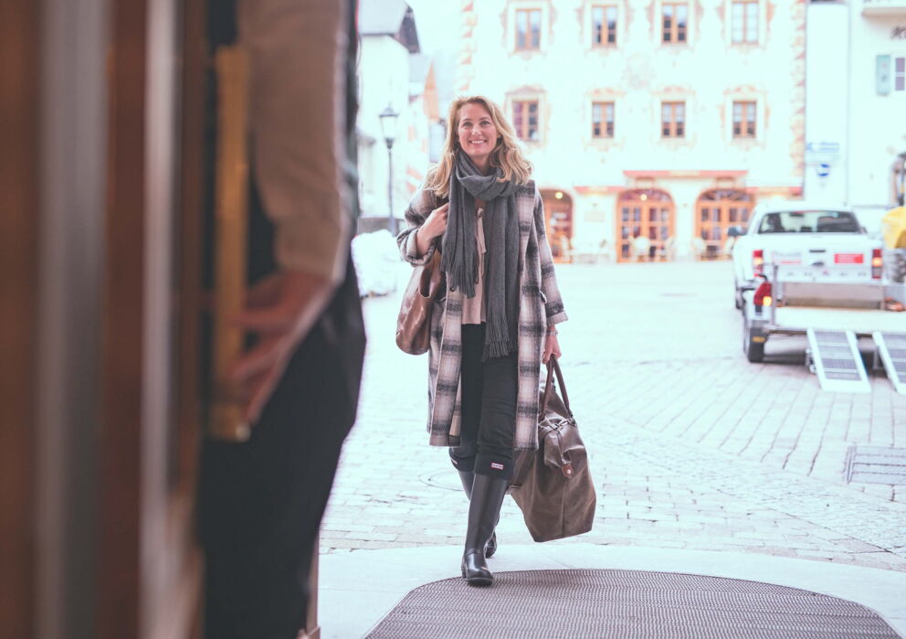 Eine Frau in warmer Kleidung und mit Reisetasche betritt das Hotel Im Weissen Rössl am Wolfgangsee