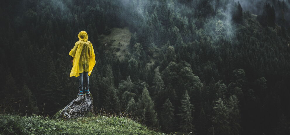 Person mit einem gelben Regenponcho auf einem Stein stehend auf einem Berg