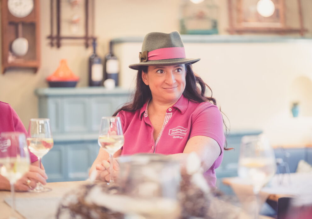 Frau mit rosafarbenem Shirt und rosa Hut mit einem Glas Wein