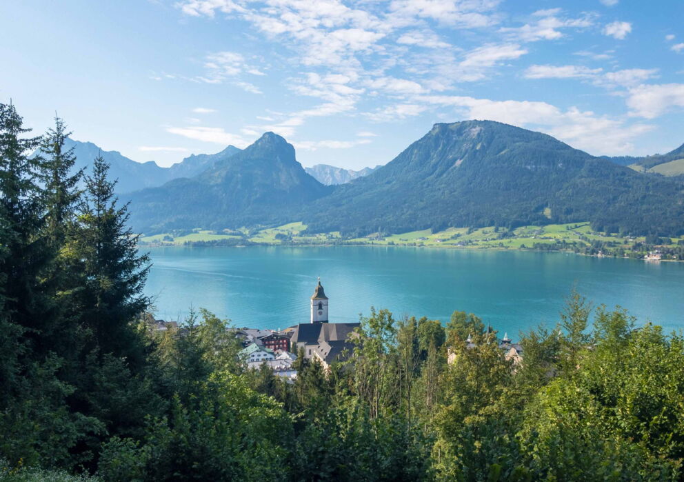 Church tower of Sankt Wolfgang in front of Lake Wolfgangsee and the surrounding mountains of the Salzkammergut region