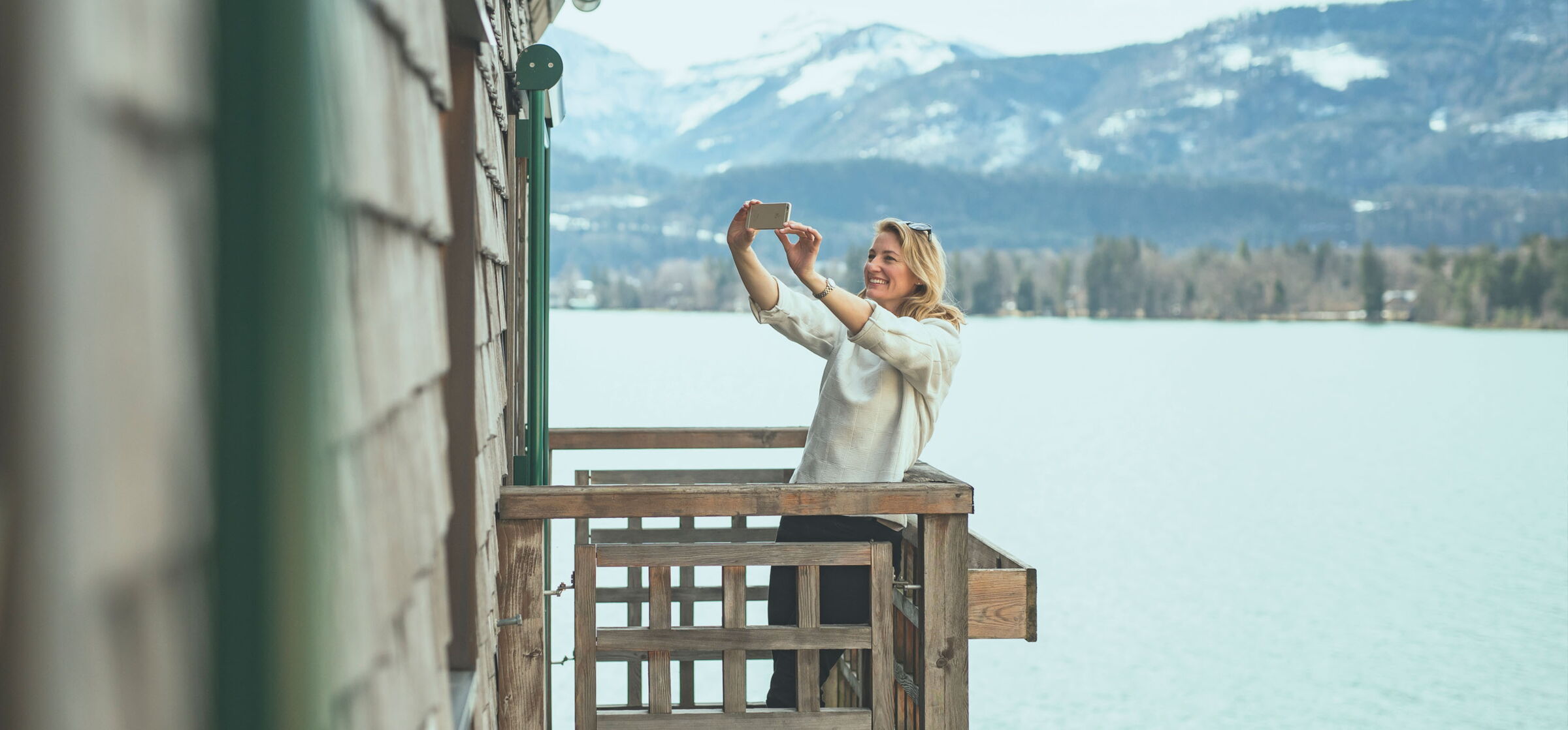 Eine Frau macht auf ihrem Balkon ein Selfie mit Blick auf den Wolfgangsee.