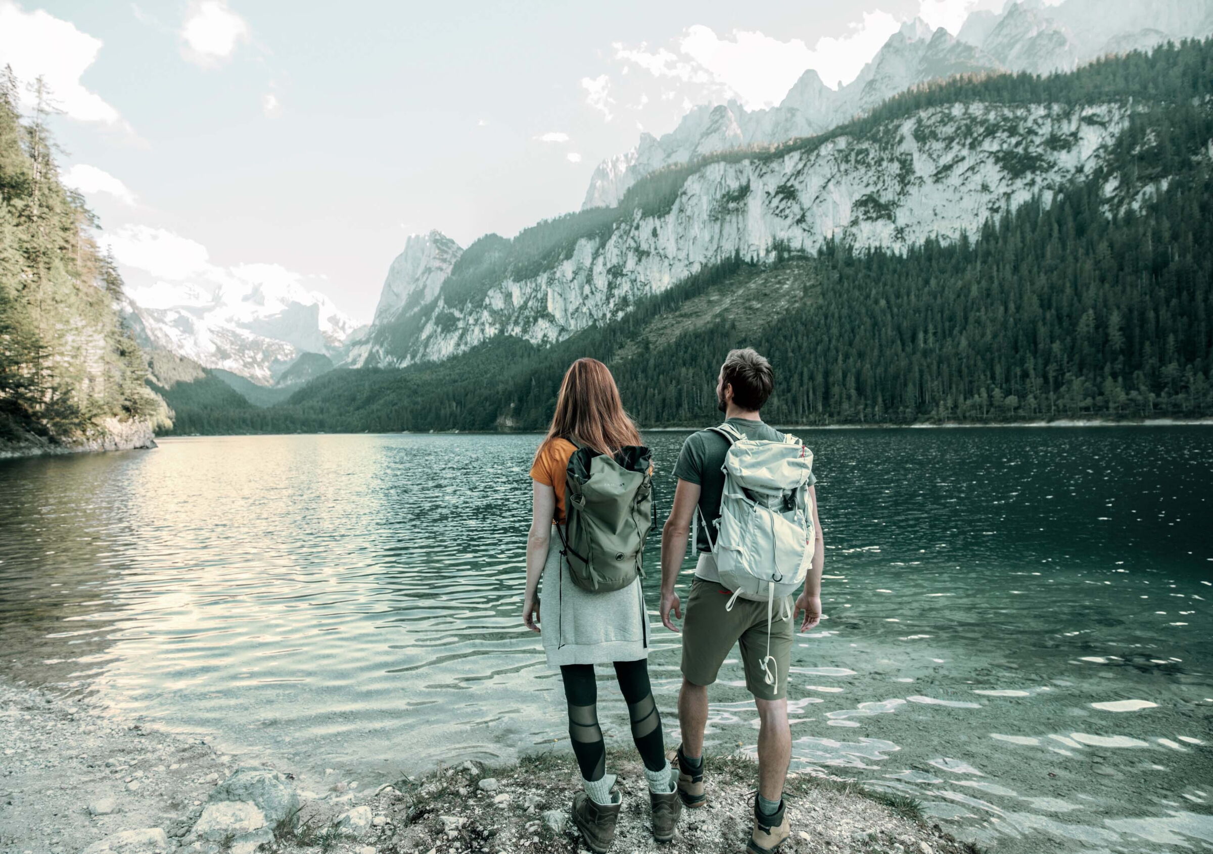 Eine Frau und ein Mann stehen an einem See, sie tragen Wander ausrüstung.