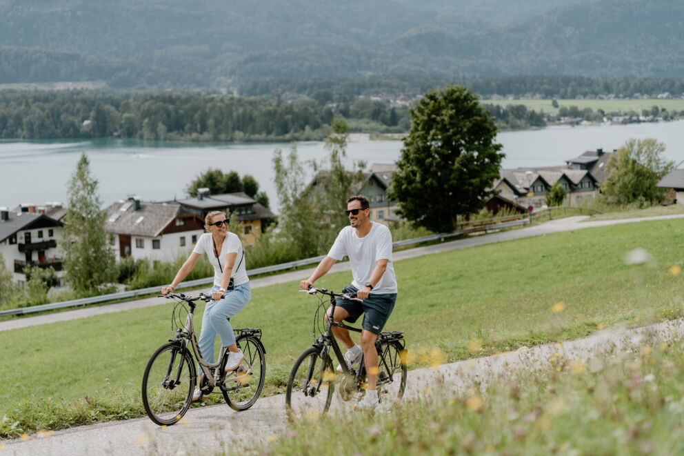 Paar beim Radfahren am Wolfgangsee mit Blick auf See und Berge, die ideale Radtour im Salzkammergut.