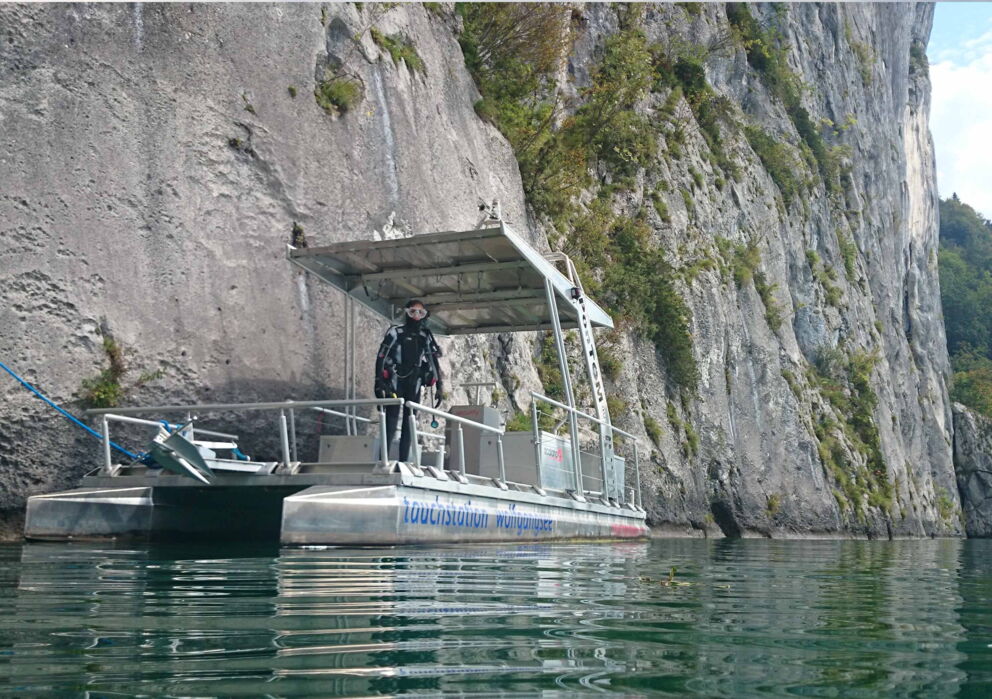 Taucher auf einem Boot vor einer riesigen Felswand am Wolfgangsee