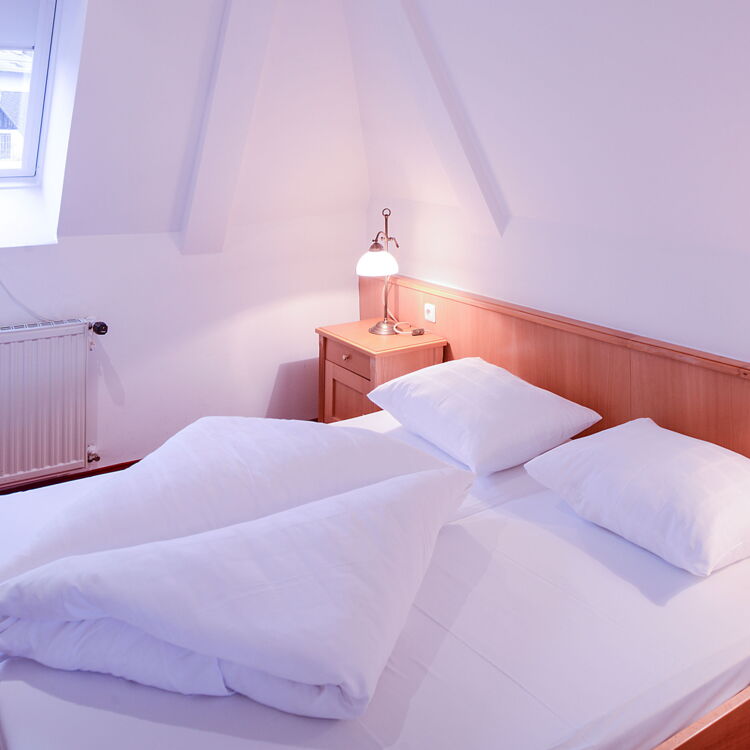 Helles weiß gestrichenes Schlafzimmer mit rotem Teppichboden und Dachschrägen verfügt über ein bequemes Doppelbett sowie Nachtischen und Bettlampen