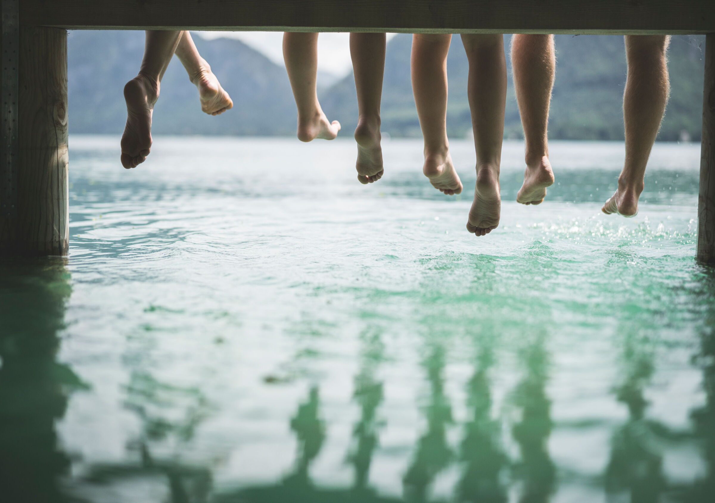 Several people sitting on a jetty with their feet dangling down above the water surface